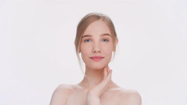 Young blonde woman softly touches her face and smiles widely