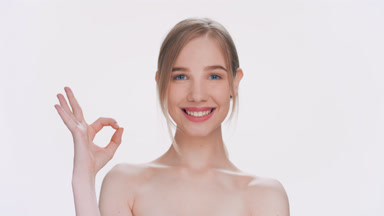 Young woman makes an ok gesture, looks at the camera and smiles