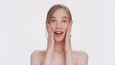 Blonde girl lays palms on her cheeks and make surprised emotion