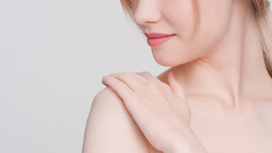 Blonde woman touches her shoulder looks at the camera and smiles
