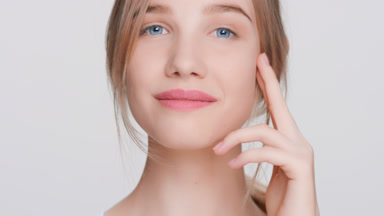 Blonde woman gently touches her face with tips of her fingers