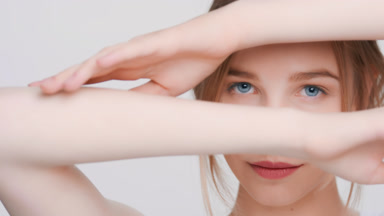 Blonde woman touches her forearm skin and looks at the camera