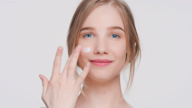 Young woman makes a smear of a cream on her face