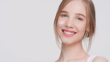 Young woman applying moisturizing cream on her face