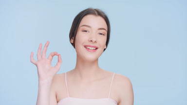 Young brunette woman looks at camera and makes an ok hand sign