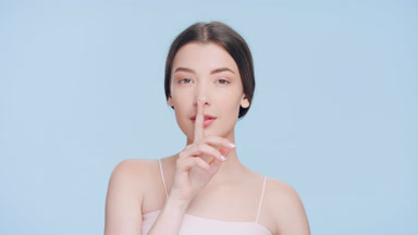 Young brunette woman looks at the camera and makes a silent sign