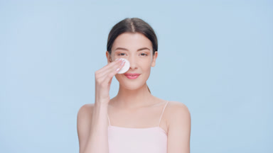 Young brunette woman applies skincare product using a cotton pad