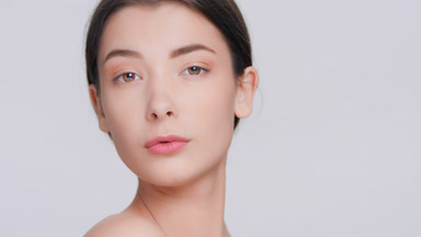 Young woman slowly looks up at camera and turns a bit on grey bg