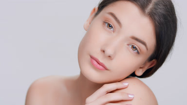Young woman softly touches her shoulder and looks at camera