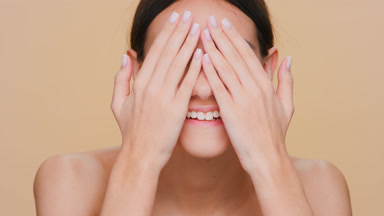 Girl looks at camera, laughs and covers eyes with her palms