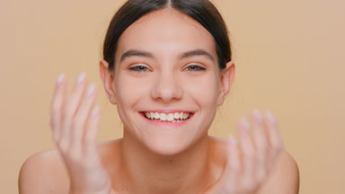 Woman looks at camera, smiles and covers her eyes with hands