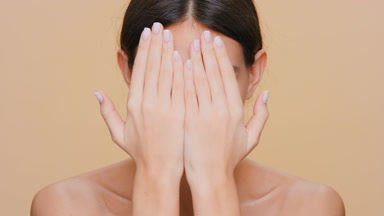 Young woman uncovers her face with her hands and looks at camera