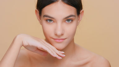 Young woman with perfect skin touches her face, looks at camera