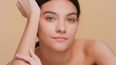 Brunette woman looks at camera and softly touches her hand skin