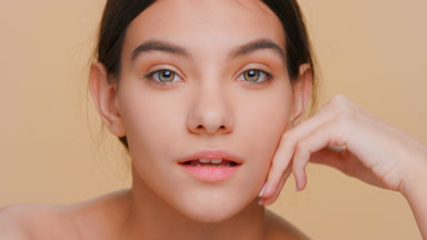 Young woman with pure skin looks at camera and touches her face