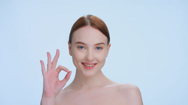 Ginger woman makes an ok sign, looks at the camera and smiles
