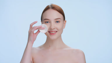 Young ginger woman applies skin care product using a cotton pad