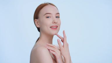 Ginger woman touches her face with pleasure and looks at camera