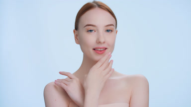 Ginger woman touches her face, looks at camera and smiles