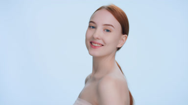 Ginger woman turn her body away, looks at camera and smiles