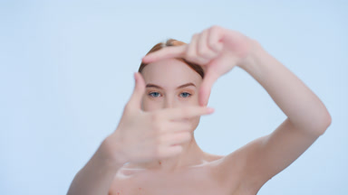 Young redhead woman looks at the camera through the finger frame