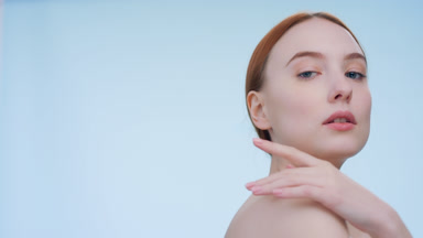 Low-angle portrait of young woman touch her body and looks away