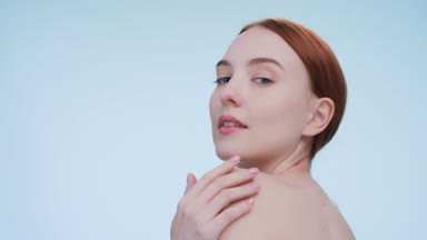 Young woman gently touches her shoulders and looks at camera