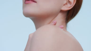 Young woman touches her neck and looks at camera over a shoulder