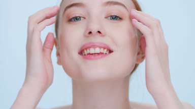 Young woman looks at camera and touches her face with both hands