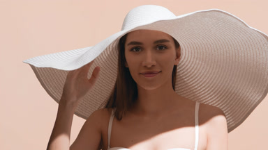 Female model in a big hat covers face from the sun with palm