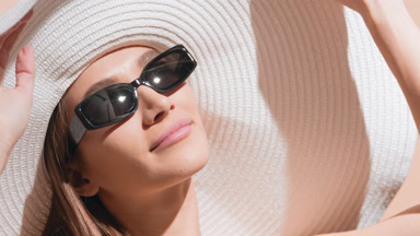 Young woman in a white hat puts sunglasses on and enjoys the sun