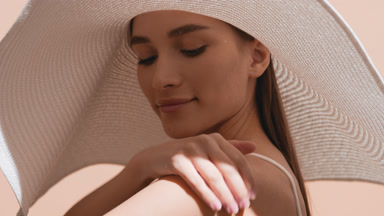 Woman in a big hat and white bra applies sunscreen on her hand