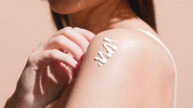 Slim woman with long dark hair applies sunblock on her shoulder