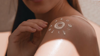 Woman in white hat and swimwear puts sunscreen on her shoulder