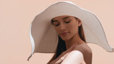 European woman in a big white hat puts sunblock on her shoulder