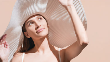 Woman in a hat applies sun cream on her body and enjoys the sun