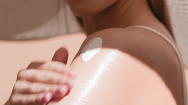 Woman in a big hat thoroughly applies sunscreen on her shoulder