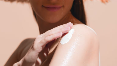 Woman in a hat applies spf cream on shoulder and enjoys the sun