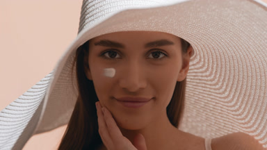 Woman with a smear of sunscreen on her cheek touches her neck