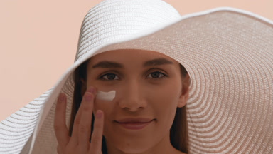 Woman smears sunscreen on her cheek and enjoys the sun smiling