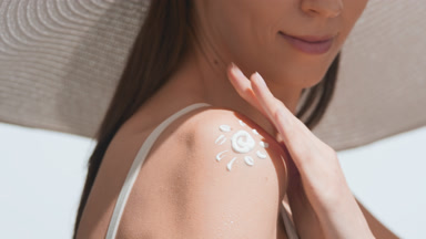 Young woman in a big white hat applies sunscreen on her shoulder
