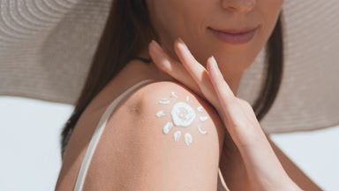 Young woman applying sunscreen on her shoulder smiles to the sun