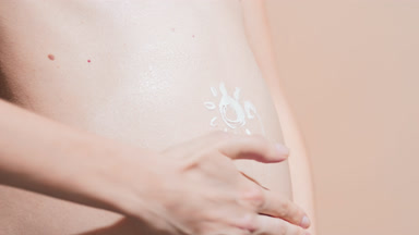 Pregnant woman in a white bra putting sunblock on her belly