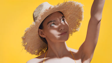 Woman in a straw hat covers her face from the sun with her palm