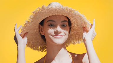 Young Caucasian woman puts a straw hat on her head and smiles