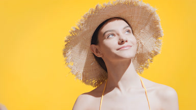 Young pretty woman puts a straw hat on her head and looks upward