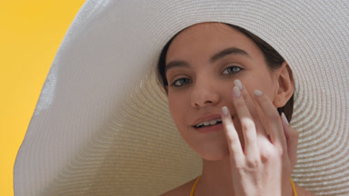 Girl in big white hat turns to the camera and touches her cheek