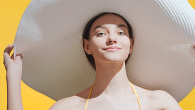 Young woman puts a big white hat on enjoying the sun and smiling