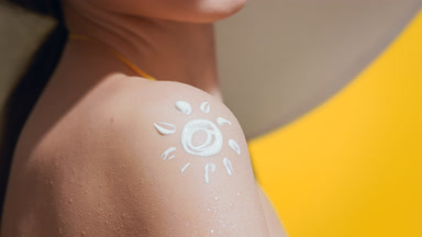 Woman in a big white hat applies sunscreen on her shoulder