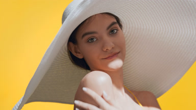 Young woman in a big white hat puts sunscreen on her shoulder